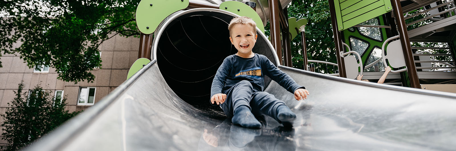 A young boy exists a large tube slide with a big smile on his face.